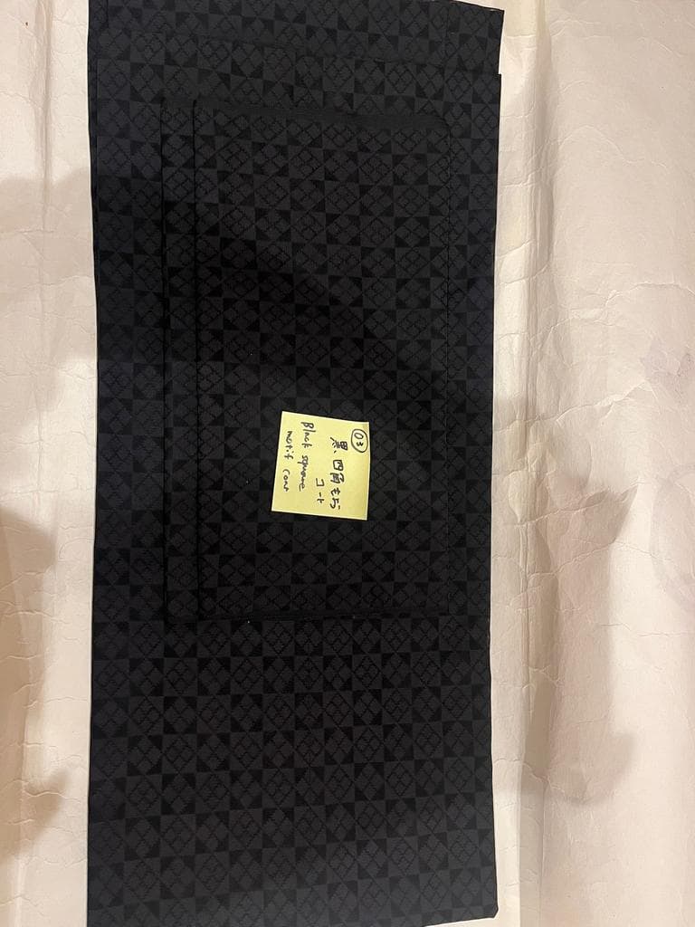 Folded black coat with geometric pattern and a note.